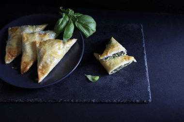 Geleneksel Yunan mutfağı. Spanakopita, ıspanaklı gevrek fillo hamur işi üçgeni, siyah arka planda beyaz peynir. Tam üstte. Boşluğu kopyala.