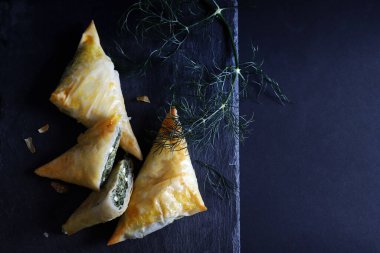 Geleneksel Yunan mutfağı. Spanakopita, ıspanaklı gevrek fillo hamur işi üçgeni, siyah arka planda beyaz peynir. Tam üstte. Boşluğu kopyala.