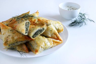 Geleneksel Yunan mutfağı. Spanakopita, beyaz arka planda ıspanak, feta, dereotu ve tzatziki soslu çıtır fileto. Tam üstte. Boşluğu kopyala.