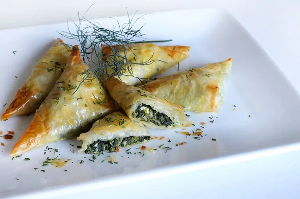 Geleneksel Yunan mutfağı. Spanakopita, ıspanaklı gevrek fillo hamur işi üçgeni, beyaz arka planda beyaz peynir. Tam üstte. Boşluğu kopyala.