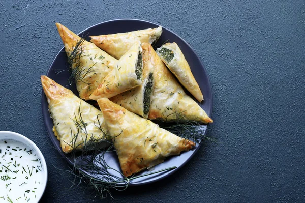 Geleneksel Yunan mutfağı. Spanakopita, gri arka planda ıspanak, feta, dereotu ve tzatziki soslu çıtır fileto. Tam üstte. Boşluğu kopyala.