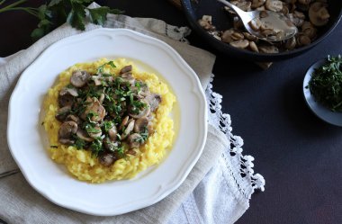 Mantarlı leziz safran risotto ve beyaz tabakta maydanoz. Geleneksel İtalyan pilavı. Tam üstte.