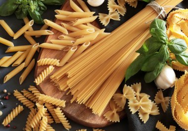 Various types of Italian pasta with vegetables and herbs on gray background. Overhead view. Cooking concept. Copy space. clipart