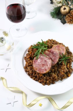 Bir tabakta mercimek ve beyaz arka planda izole edilmiş bir bardak kırmızı şarap ile Cotechino. Noel süsleri. Noel tatili. İtalyan yemeği konsepti. Genel Görünüm.