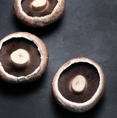 Taze çiğ portobello mantarları koyu arka planda izole edilmiş. Sağlıklı ve vejetaryen yemekleri. Tam üstte.