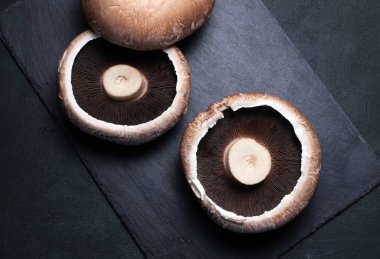 Taze çiğ portobello mantarları koyu arka planda izole edilmiş. Sağlıklı ve vejetaryen yemekleri. Tam üstte.