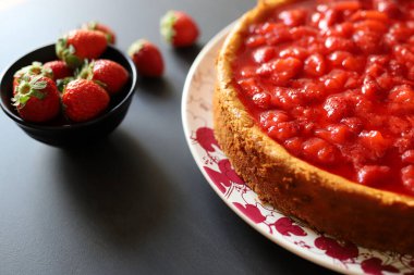 Fırın konsepti. Masada çilek soslu ev yapımı cheesecake. Arka planda taze çilekler.