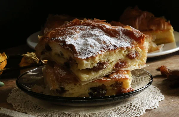 stock image Traditional greek cuisine. Delicious Bougatsa, phyllo pastry filled with cream and sultanas, garnished with powdered sugar. Close-up.