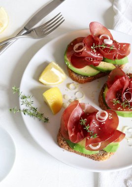 Beyaz arka planda Bresaola (tütsülenmiş et) ile avokado tostu. Sağlıklı gıda konsepti. Genel bakış. Boşluğu kopyala.