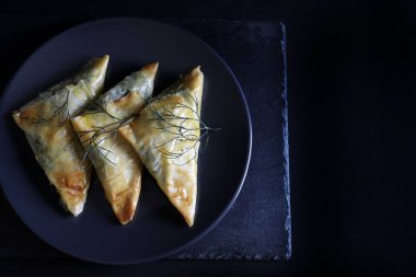 Geleneksel Yunan mutfağı. Spanakopita, siyah arkaplanda ıspanak ve feta olan çıtır fileto üçgenleri. Tam üstte. Boşluğu kopyala.