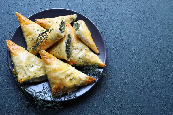 stock image Traditional Greek cuisine. Spanakopita, crispy phyllo pastry triangles with spinach and feta on gray background. Directly above. Copy space.