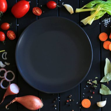 Sağlıklı gıda ya da diyet konsepti. Sebzeler, baharatlar ve otlar boş bir tabağın etrafında siyah tahta bir masanın üzerinde. Uzayı kopyala Genel Görünüm.