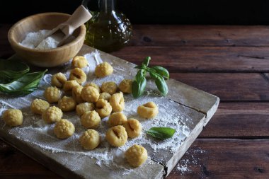 Geleneksel İtalyan yemekleri. Mutfaktaki un tahtasının üzerinde pişmemiş taze ev yapımı gnocchi ve arka planda taze fesleğen yaprakları..