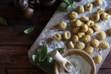 Geleneksel İtalyan yemekleri. Mutfaktaki un tahtasının üzerinde pişmemiş taze ev yapımı gnocchi ve arka planda taze fesleğen yaprakları..