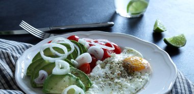 Yağda yumurta ve avokado, domates, beyaz tabakta sebze. Sağlıklı kahvaltı kavramı. Genel manzara, düz yatış. Boşluğu kopyala.