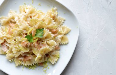 Füme somonlu Farfalle makarna, krema sosu ve beyaz tabakta limon. Genel bakış. İtalyan yemeği kavramı. Boşluğu kopyala.