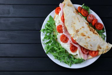 Jambonlu İtalyan piadinası, mozzarella, salata ve domatesler ahşap arka planda izole edilmiş. Genel bakış. Boşluğu kopyala.