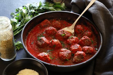 Domates soslu ev yapımı köfteler ve arka planda bir tavada servis edilen baharatlar. Genel Görünüm.