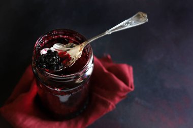 Koyu arka planda izole edilmiş neredeyse boş bir cam kavanozun üzerinde duran çilek reçelli kaşık. Genel görünüm, boşluğu kopyala.