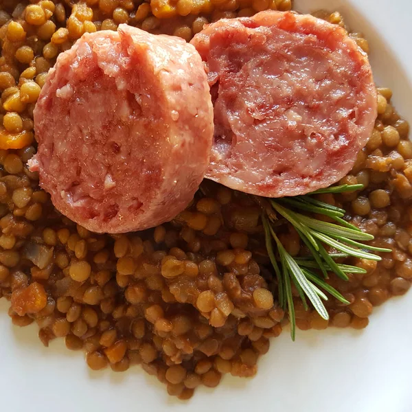 New Year\'s Eve meal Italian style. Two slices of cotechino (pork sausage), lentils and rosemary on white plate. Overhead view, close-up. Holiday season.