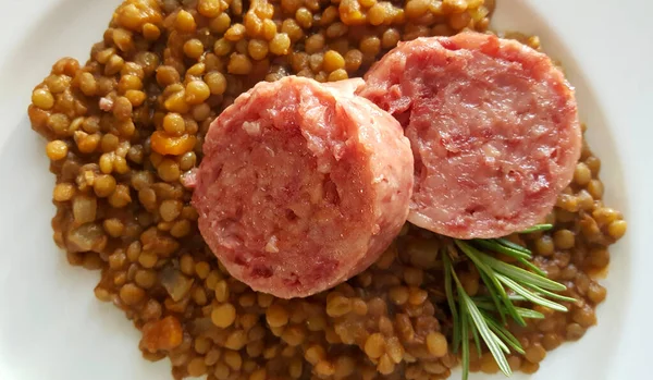 New Year\'s Eve meal Italian style. Two slices of cotechino (pork sausage), lentils and rosemary on white plate. Overhead view, close-up. Holiday season.