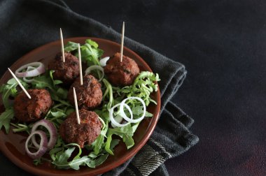 Koyu bir arka planda izole bir tabakta roket yapraklı leziz kızarmış köfteler. Yukarıdan bak. Boşluğu kopyala.