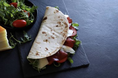 Geleneksel İtalyan piadinası, jambonlu, peynirli, salatalı ve domatesli siyah arka planda. İtalyan yemek sokağı. Genel bakış. Boşluğu kopyala.