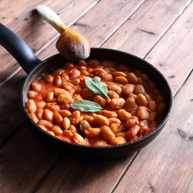 Domates soslu beyaz fasulyeler ve ahşap bir arka planda otlar. Genel bakış. Boşluğu kopyala.