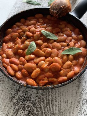 Domates soslu beyaz fasulyeler ve ahşap bir arka planda otlar. Genel bakış. Boşluğu kopyala.