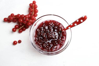 Ev yapımı reçel konsepti. Cam kasede kırmızı frenk üzümü reçeli ve beyaz arka planda taze frenk üzümü. Genel bakış. Boşluğu kopyala.