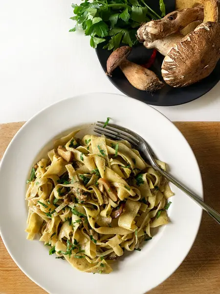 İtalyan yemeği. Porcini mantarlı Tagliatelle ve beyaz arka planda bir tabakta maydanoz. Ev yapımı sonbahar yemeği. Genel Görünüm.