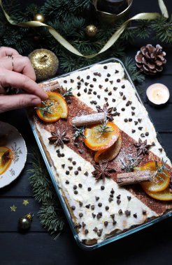 Lezzetli İtalyan portakallı tiramisusunu mascarpone peyniri ile süsleyen bir kadın, koyu arka planda parmak bisküvisi. Noel süsü. Tatil sezonu. Genel Görünüm.