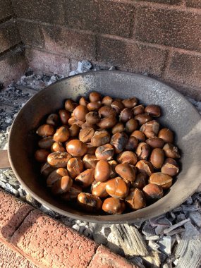 Kestaneler demir tavada ateşte pişiyor. Kızarmış kestane. Sonbahar meyvesi. Sonbaharda açık hava yemekleri. Genel Görünüm.