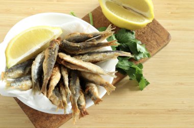 Tahta arka planda beyaz bir kasede limonlu kızarmış sardalya. Genel bakış. Boşluğu kopyala.