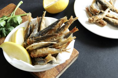 Gri arka planda beyaz bir kasede limonlu kızarmış sardalya. Genel Görünüm.