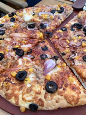 Tahta kesme tahtasının üzerinde çeşitli malzemelerle dilimlenmiş lezzetli bir pizza. İtalyan yemeği. Genel Görünüm.