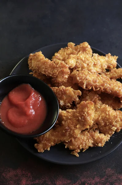 stock image  Plate with fried chicken nuggets with ketchup on dark background. Tasty fast food. Overhead view. Copy space.