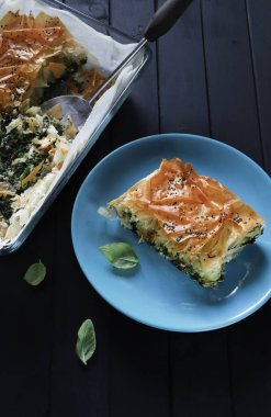 Geleneksel Yunan mutfağı. Spanakopita, blu tabakta ıspanaklı ve peynirli Yunan usulü hamur işi turtası, siyah arkaplan. Yakın plan.. 