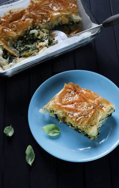 Geleneksel Yunan mutfağı. Spanakopita, blu tabakta ıspanaklı ve peynirli Yunan usulü hamur işi turtası, siyah arkaplan. Yakın plan.. 