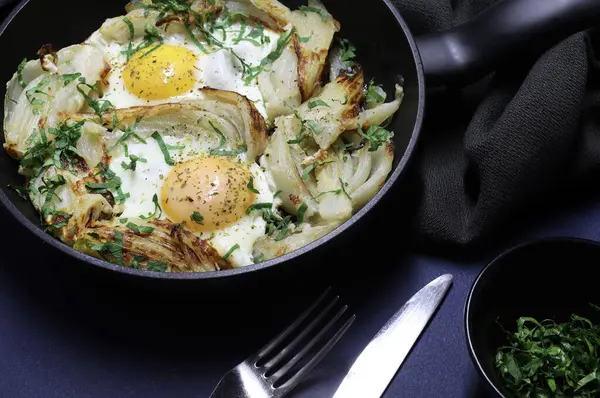 Homemade fried eggs and fennel with herb in an iron pan on dark background. Healthy and vegetarian food. Overhead view.