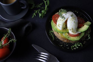 Avokado tostu, haşlanmış yumurta ve siyah arka planda domates. Sağlıklı gıda konsepti. Genel Görünüm.