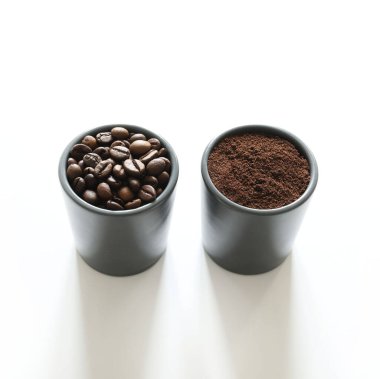 İki gri kahve fincanı, kahve çekirdeği ve beyaz arka planda izole edilmiş öğütülmüş kahve. Genel bakış. Boşluğu kopyala.