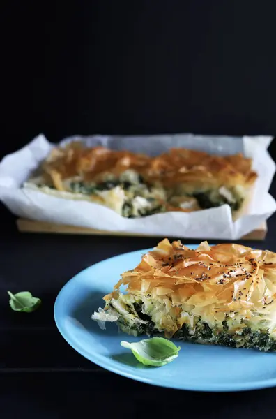Traditional greek cuisine. Spanakopita, a piece of greek phyllo pastry pie with spinach and feta cheese filling on blu plate.