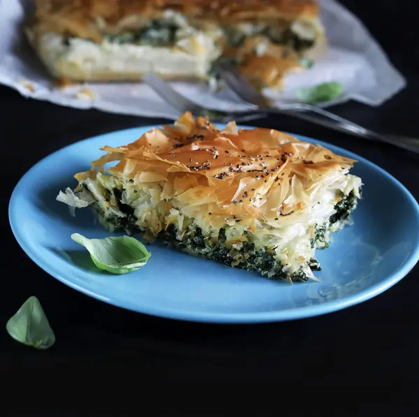 Traditional greek cuisine. Spanakopita, a piece of greek phyllo pastry pie with spinach and feta cheese filling on blu plate.