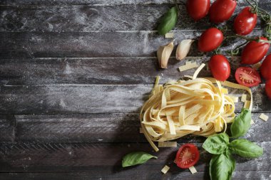 İtalyan makarnası. Çiğ makarna, domates, taze fesleğen ve ahşap arka planda sarımsak. Sağlıklı gıda konsepti. Genel bakış. Boşluğu kopyala.