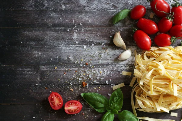 Italian pasta. Raw pasta, tomatoes, fresh basil and garlic on wooden background. Healthy food concept. Overhead view. Copy space.