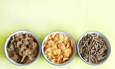 Pastel yeşil arka planda izole edilmiş kaselerdeki farklı kuru kahvaltı gevrekleri. Genel bakış. Boşluğu kopyala.