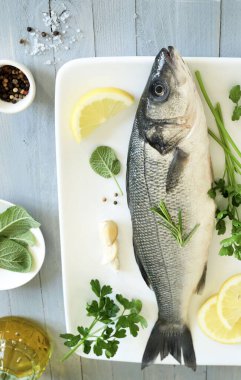 Beyaz bir tabakta baharat ve limon ile taze deniz levreği, gri ahşap arka plan. Deniz ürünleri. Tam üstte.