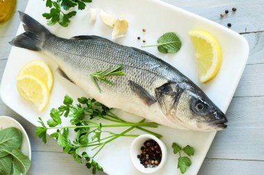 Beyaz bir tabakta baharat ve limon ile taze deniz levreği, gri ahşap arka plan. Deniz ürünleri. Tam üstte.
