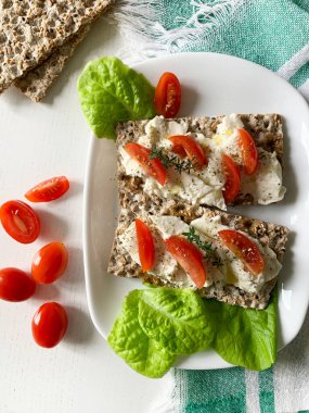 Taze otlu peynir, domates dilimleri ve beyaz arka planda susam tohumlu topak kraker. Sağlıklı gıda konsepti. Tam üstte.